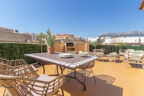 An outdoor patio with a table and chairs, a potted plant, and a view of buildings and mountains in the background. - Apartamento Paola - Costa CarpeDiem (Calp)