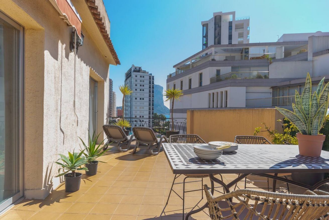 Terraza en la azotea con una mesa y sillas, rodeada de plantas en macetas.
