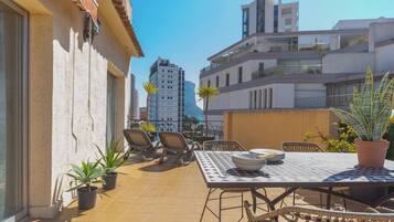 Terraza en la azotea con una mesa y sillas, rodeada de plantas en macetas.