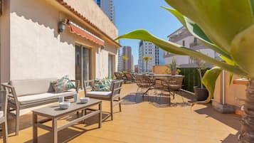 An outdoor patio area with a sofa, dining table, chairs, and a small garden.