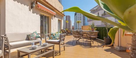 Un patio al aire libre con sofá, mesa de comedor, sillas y un pequeño jardín.