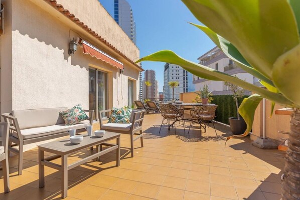 Un espace extérieur aménagé en terrasse, avec un canapé, une table à manger, des chaises et un petit jardin.