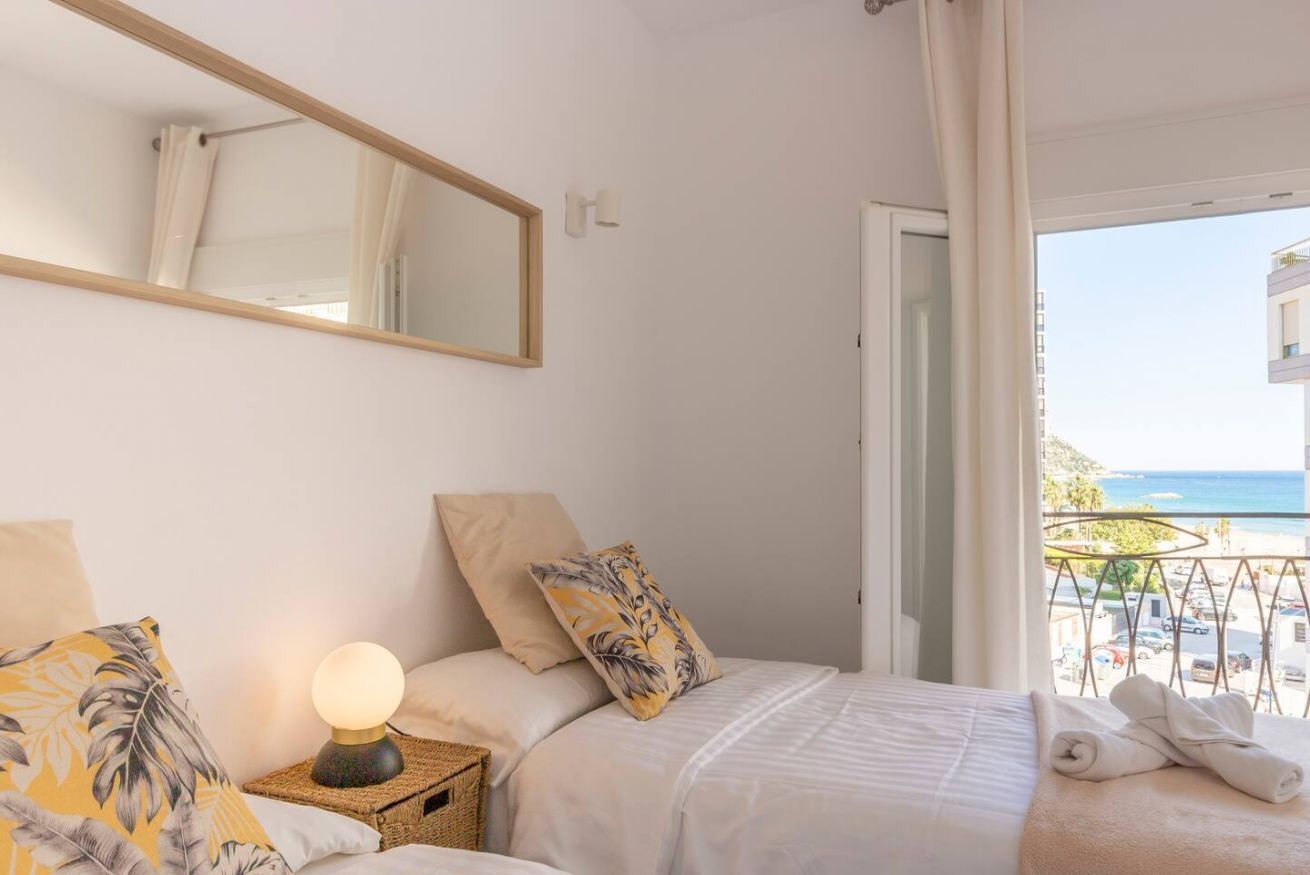 Een hotelkamer met een bed, een bedlamp, een spiegel en uitzicht op zee.