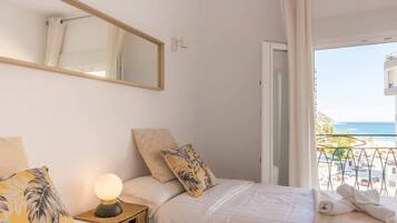 Een hotelkamer met een bed, een bedlamp, een spiegel en uitzicht op zee.