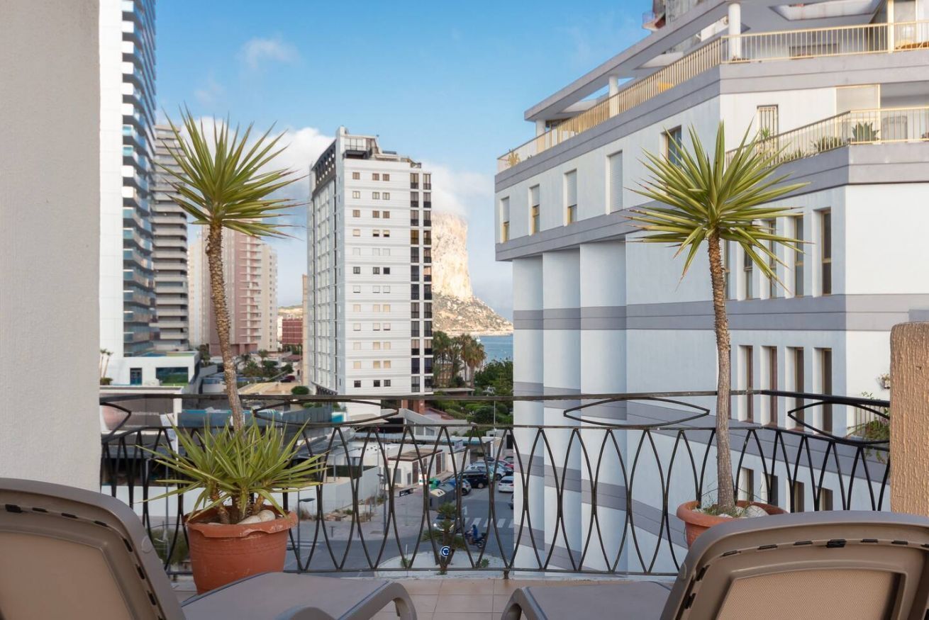 Un balcon orné de deux plantes en pot, une vue sur un paysage urbain avec de hauts immeubles et un ciel dégagé.