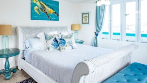 Een slaapkamer met een groot bed, een blauwe gestoffeerde bank, een plafondventilator en een raam met gordijnen.