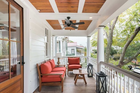 A covered porch with a ceiling fan, wooden furniture, and a view of a house in the background.