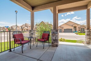 A covered outdoor seating area with two chairs and a table, overlooking a residential street with houses and a clear sky. - Hawk 3: Pet-Friendly w/ Fire pit (Fruita)