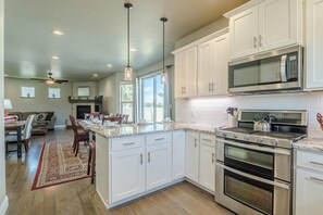 A modern kitchen with white cabinetry, stainless steel appliances, and a dining area with a red rug. - Hawk 3: Pet-Friendly w/ Fire pit (Fruita)
