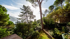 A lush garden with a wooden deck, stone wall, and a view of the sea and mountains. - Villa La Pavona Luxury Collection (Monterosso al Mare)
