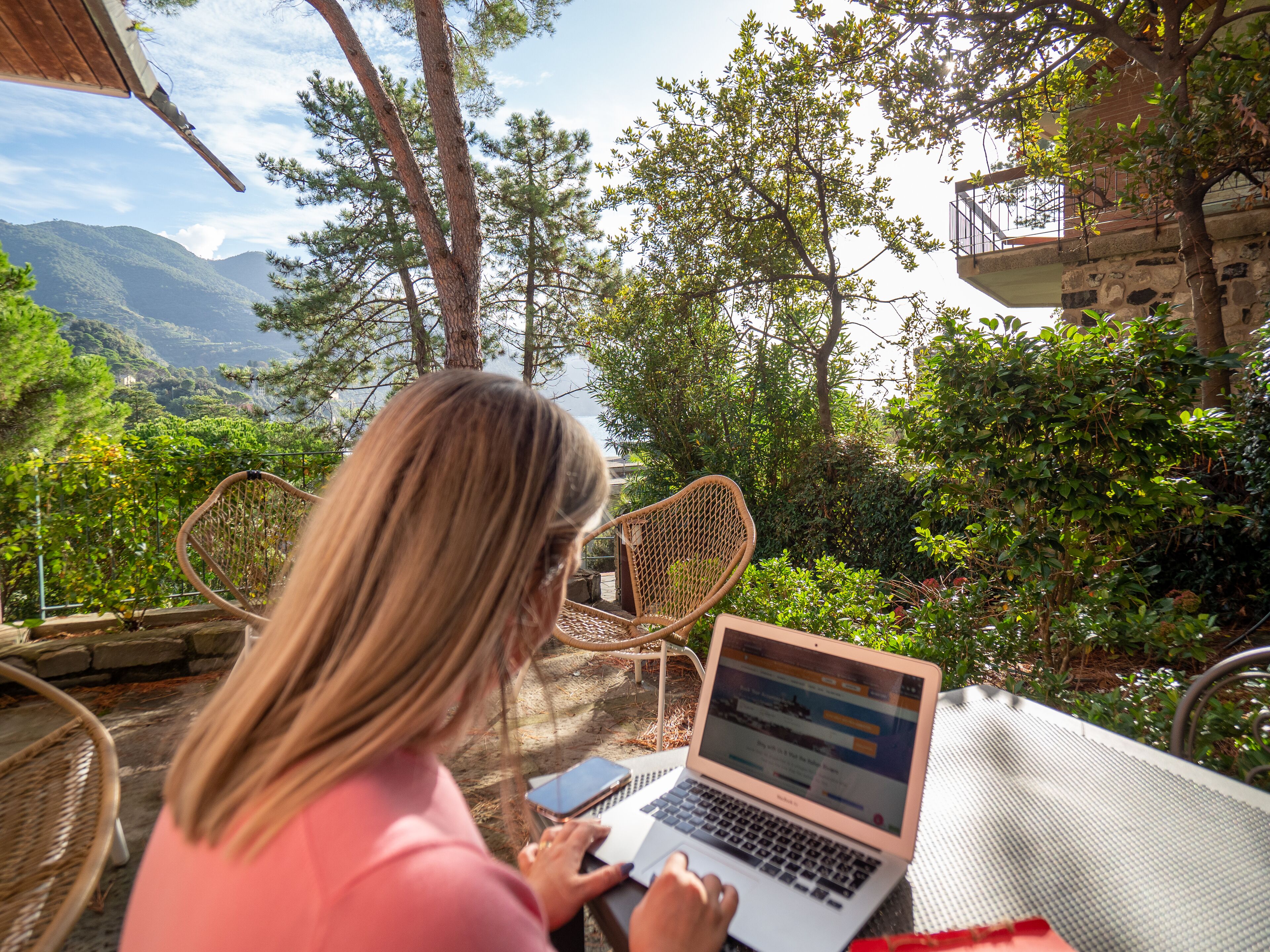 Uma pessoa usando um laptop ao ar livre, com vista para montanhas e árvores.