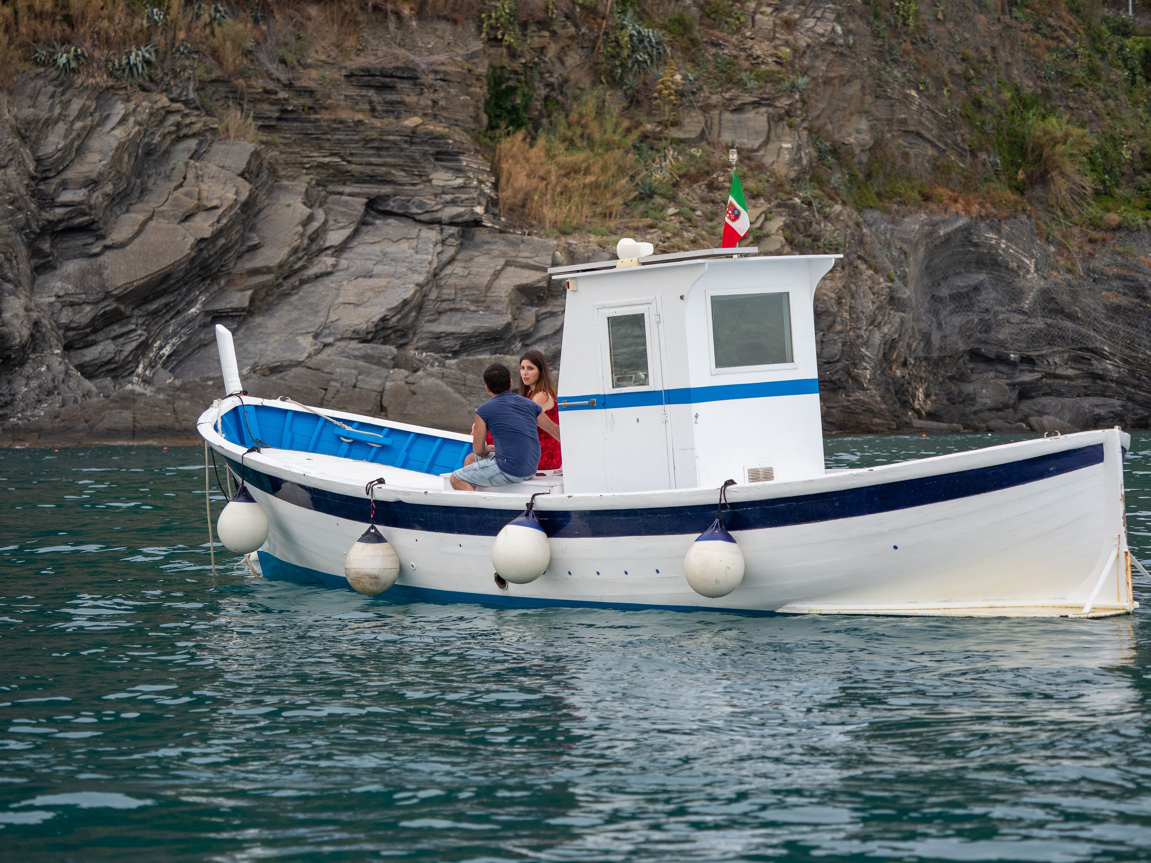 A small boat with two people on board, anchored near rocky cliffs.