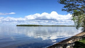 A calm lake with a rocky shoreline and a distant tree line under a clear sky.