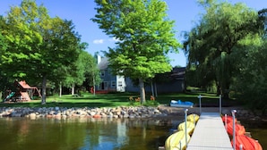 A dock with kayaks, a pond, and a house with a lawn and trees.