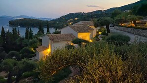 Una proprietà costiera con diversi edifici, un muro in pietra e vista sul mare e sulle colline.