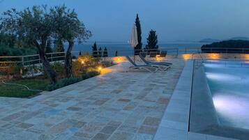 Relax by the pool surrounded by a serene patio with lounge chairs and a sun umbrella.