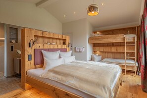 A bedroom with a large bed, a wooden headboard, a built-in shelf, a bedside table, and a bunk bed.