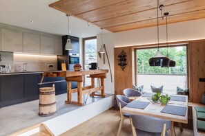 A modern kitchen with a wooden table and chairs, a large window with a view, and a rustic barrel.