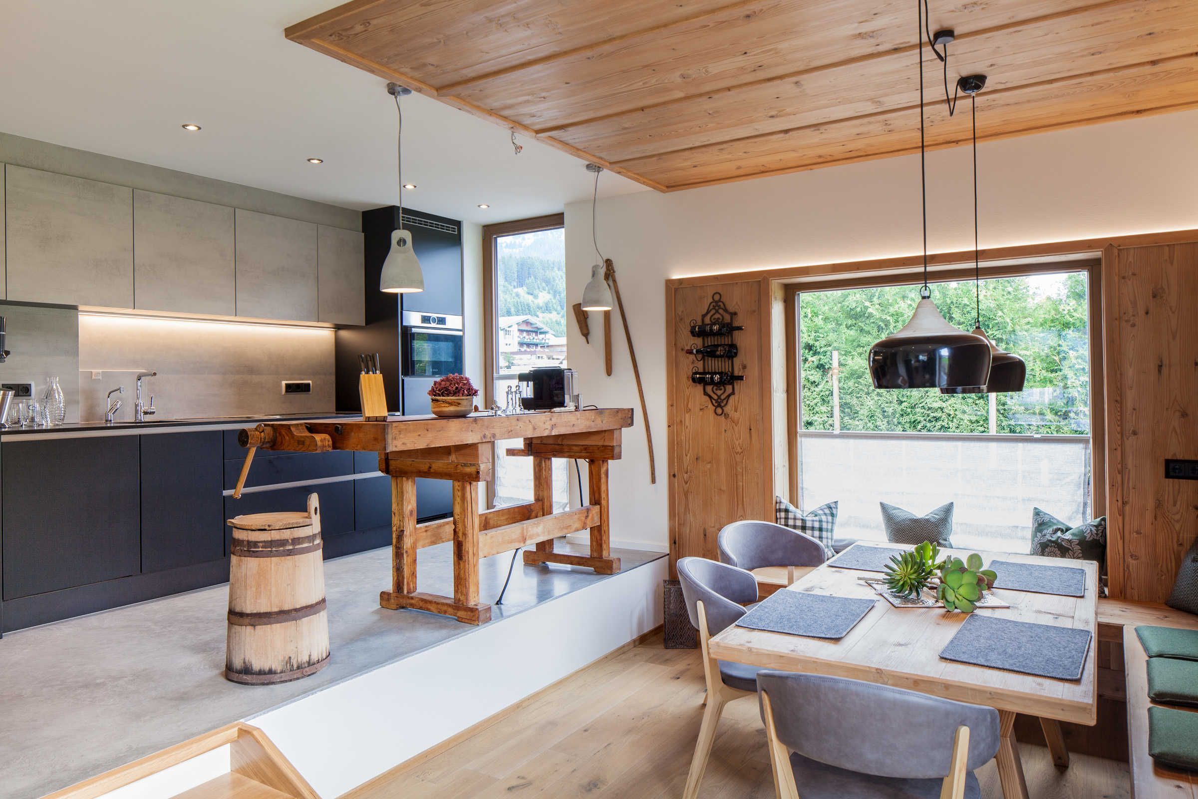 A modern kitchen with a wooden table and chairs, a large window with a view, and a rustic barrel.