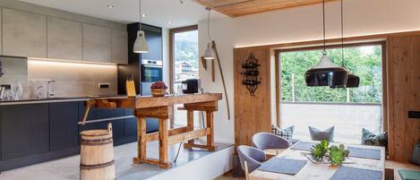 A modern kitchen with a wooden table and chairs, a large window with a view, and a rustic barrel.