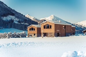 A wooden cabin with a stone facade, set against a snowy mountain backdrop.