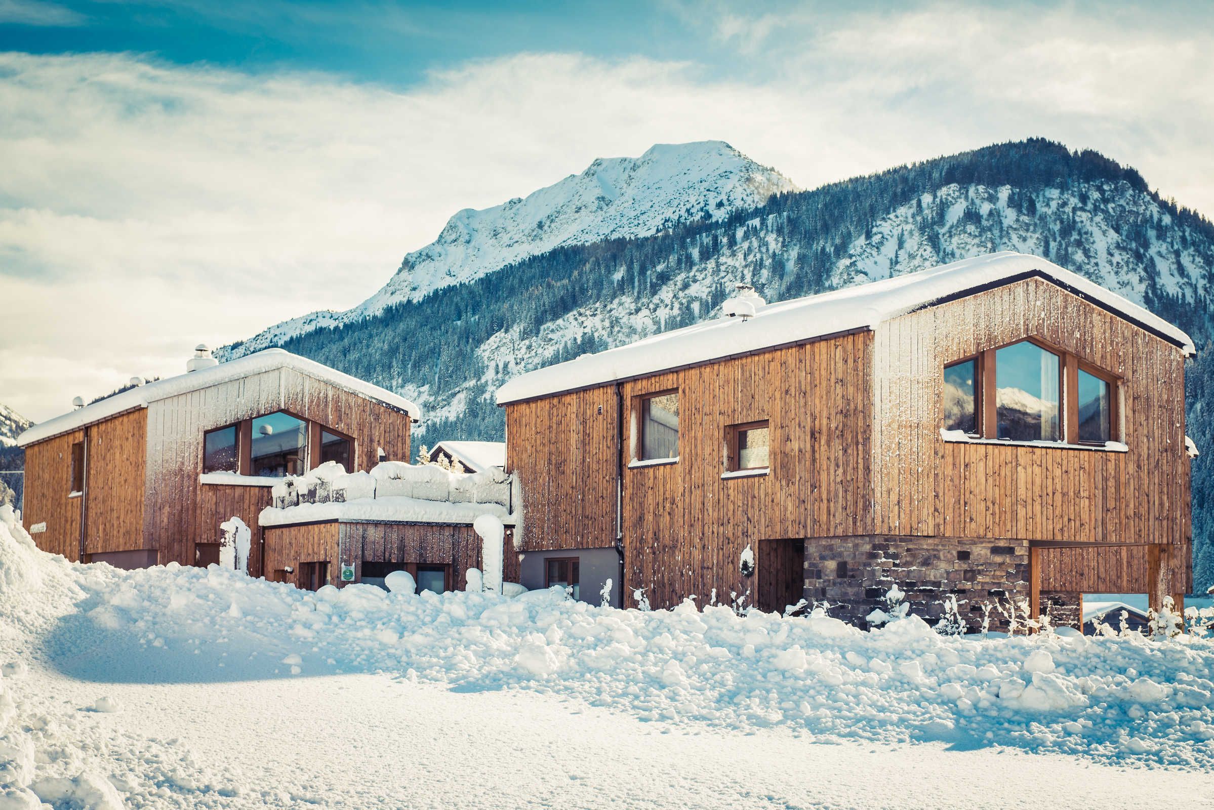 Une cabane en bois, dont le toit est recouvert de neige, se dressant sur un fond de montagnes.