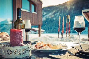 A table with food, wine, and a candle, set outdoors with mountains in the background.
