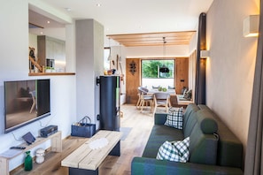 Een moderne woonkamer met een flatscreen televisie, een houten salontafel en een groene bank met geruite kussens.