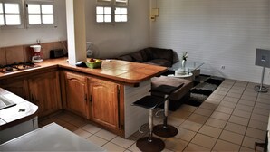 A kitchen with wooden cabinets, a countertop, a stove, a sink, and a window with blinds. - Beautiful F2, jaccuzi, near beach (5mn walk) (La Trinité)