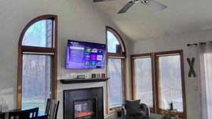 Un salon doté d’une cheminée, d’un ventilateur de plafond et d’un téléviseur fixé au-dessus de la cheminée.