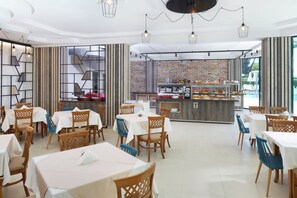 Un restaurant doté de nombreuses tables et chaises, d’un bar central et offrant une vue sur l’extérieur.
