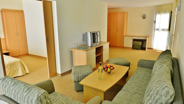A modern hotel room with a sofa, a coffee table with fruit, a TV, and a small kitchenette. - Aktinia (Nessebar)