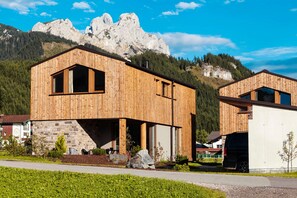 A wooden building with a large window and a stone base, set against a mountainous backdrop. - Chalet N ° 4 - Gränobel chalets (Grän)