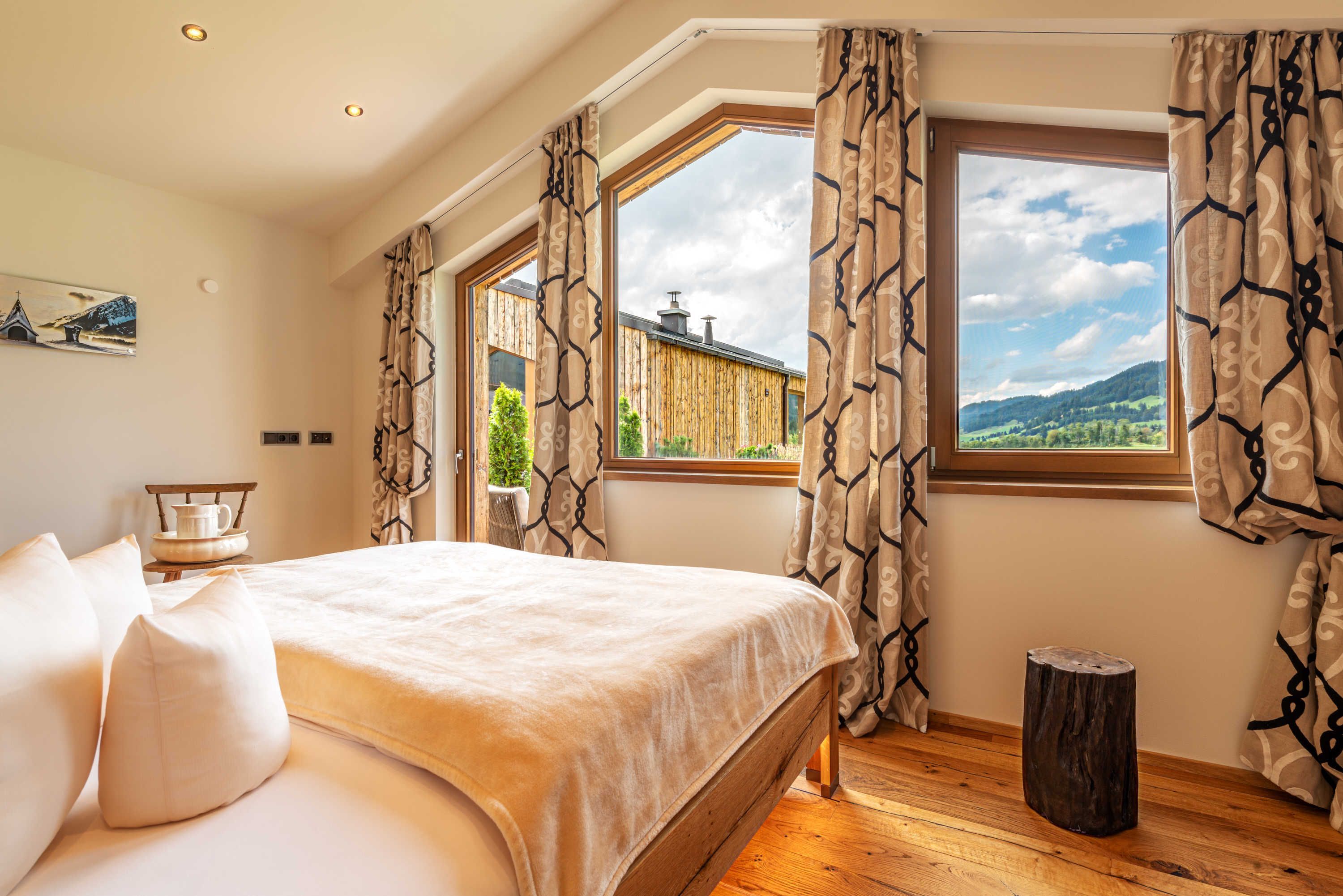 Ein Schlafzimmer mit einem großen Bett, zwei Vorhängen und einem Holzboden, sowie einem kleinen Hocker.