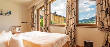 Ein Schlafzimmer mit einem großen Bett, zwei Vorhängen und einem Holzboden, sowie einem kleinen Hocker.