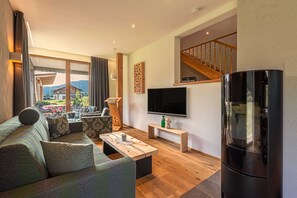 A modern living room with a sofa, coffee table, TV, and a staircase. - Chalet N ° 4 - Gränobel chalets (Grän)