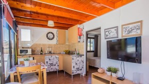 A compact kitchen with a microwave, sink, and wooden cabinets. There is a dining area with a table and chairs. A television is mounted on the wall. - Pico Colorado de Soo (Soo)