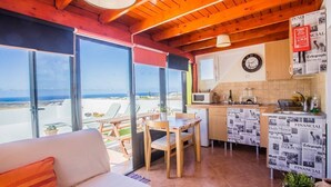 A cozy room with a sofa, a dining table, and a kitchen area with a view of the sea. - Pico Colorado de Soo (Soo)