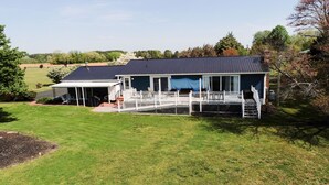 Ein Haus mit überdachter Terrasse, umzäunter Terrasse und Rasenfläche.