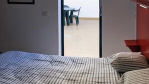 A bed with striped bedding, a tiled floor, and a view of an outdoor area with a table and chairs. - Cosy Flat in Playa San Juan with Large Patio (Guía de Isora)