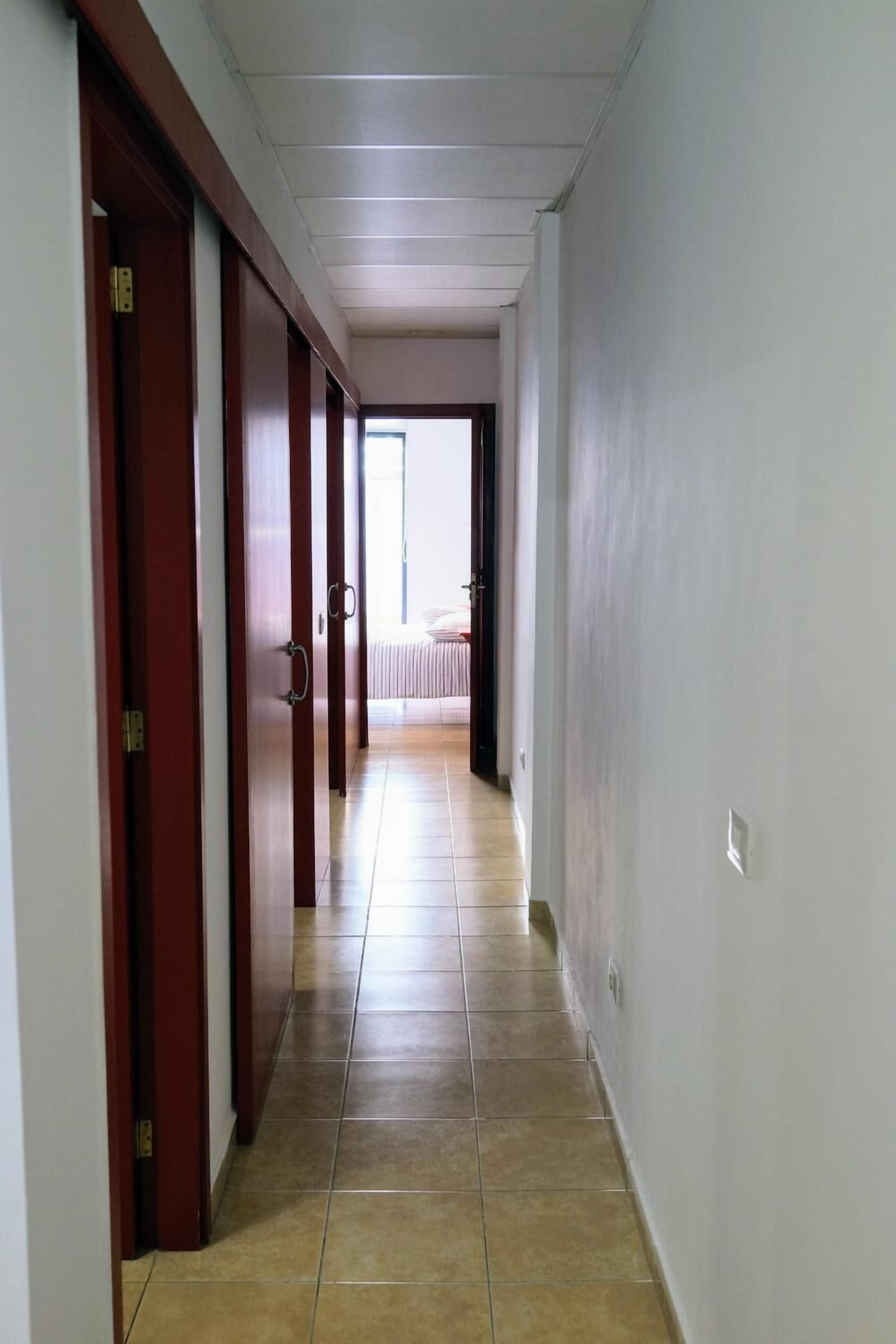 A hallway with wooden doors, a tiled floor, and a bed visible in the distance.