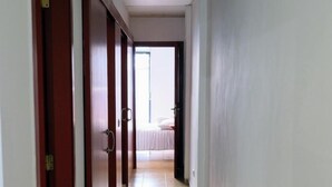 A hallway with wooden doors, a tiled floor, and a bed visible in the distance. - Cosy Flat in Playa San Juan with Large Patio (Guía de Isora)