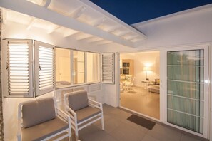 Un interior moderno con una zona de estar, una cocina visible a través de una puerta abierta y un cerramiento de vidrio corredizo que da a un espacio exterior.