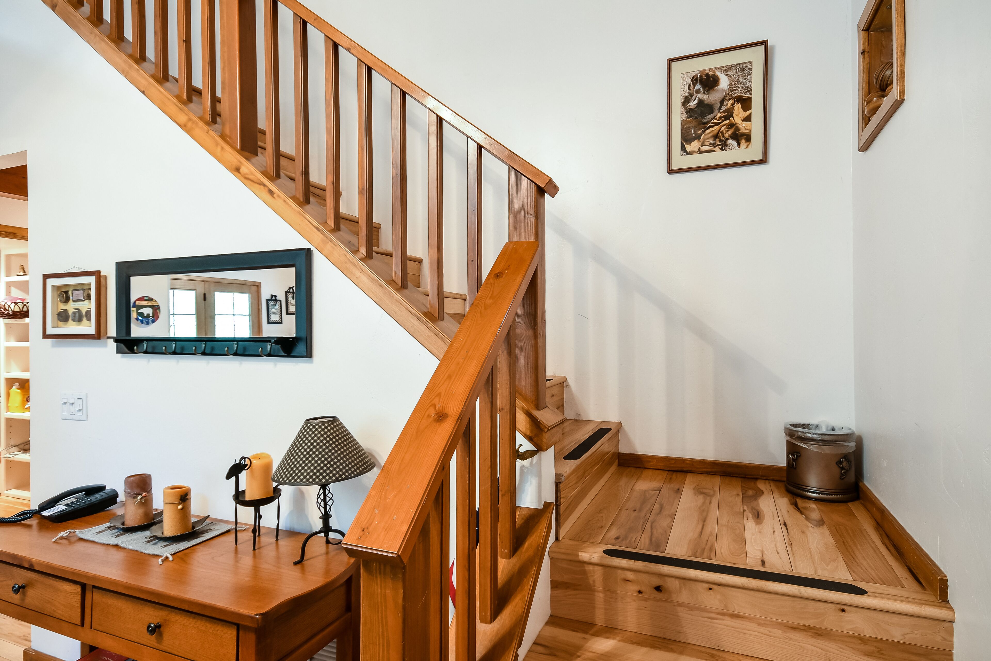 A wooden staircase with a wooden desk and a lamp, a framed picture on the wall, and a small wooden table with a container.