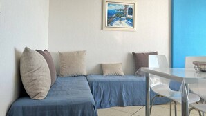 A room with a blue sofa, a small table, and a framed picture on the wall. - Seafront studio with private parking - Le Lavandou (Le Lavandou)