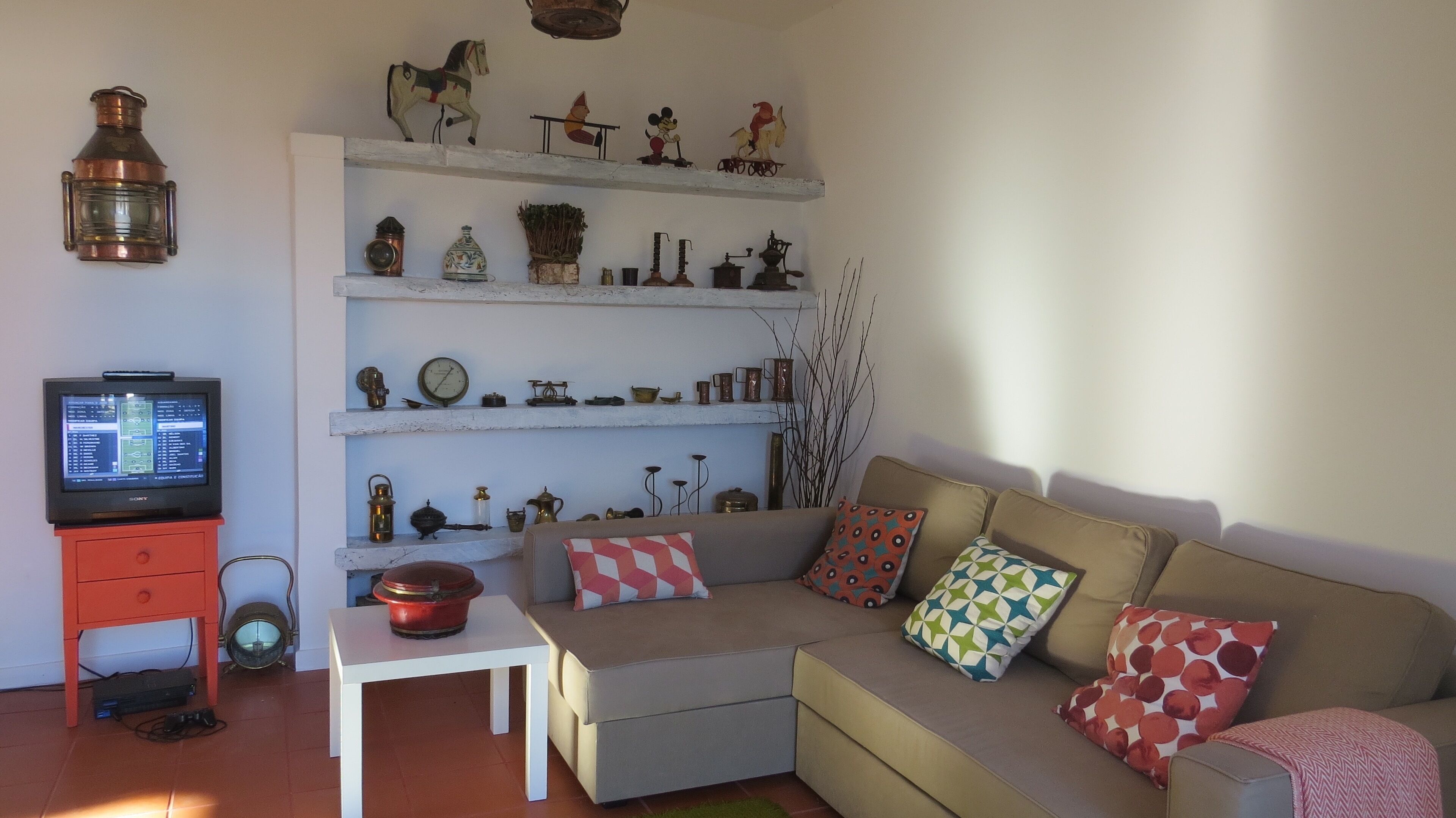 Una sala de estar con un sofá, un televisor y estanterías con varios objetos decorativos.