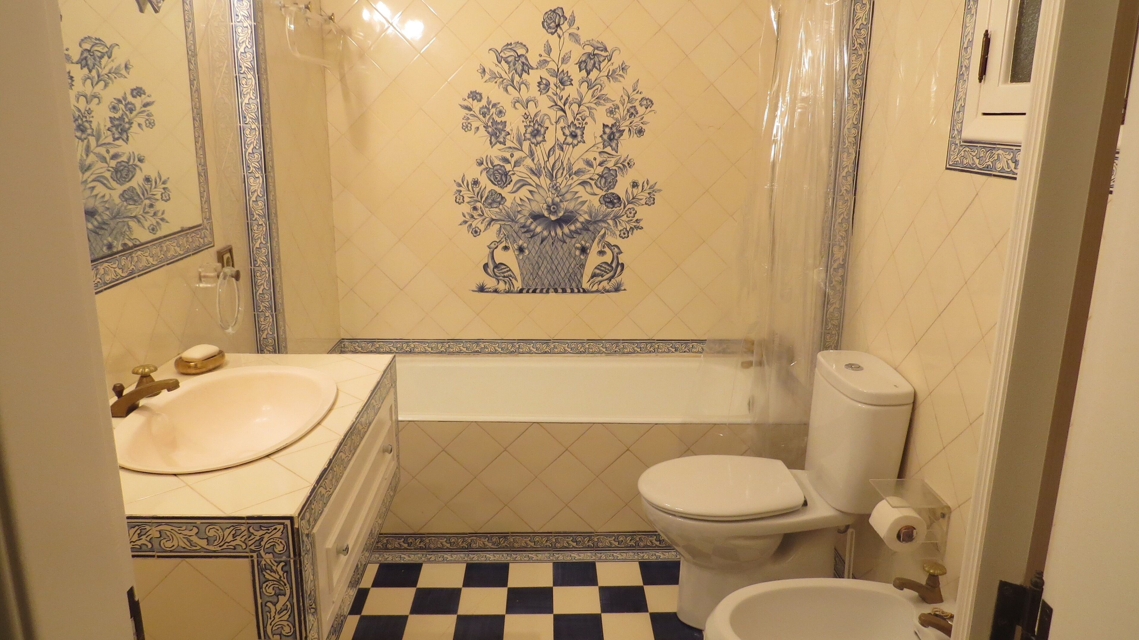 A bathroom with a sink, toilet, and bathtub. The walls have decorative tiles with a floral pattern.