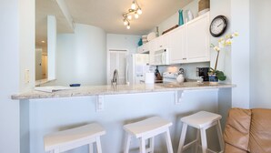 A kitchen with white cabinets, a countertop, and three white stools. - Direct Beach Front, June 20-23 OPEN! Free Beach Service, Amazing View, LazyRiver (Fort Walton Beach)
