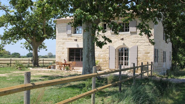 A stone building with a wooden fence, a table, and chairs outside. - Roulotte La Nanouche (Le Cailar)