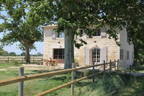 A stone building with a wooden fence, a table, and chairs outside. - Roulotte La Nanouche (Le Cailar)